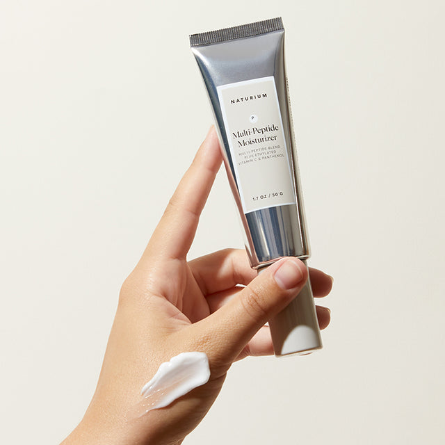 a hand holds up a tube of multi-peptide moisturizer. 